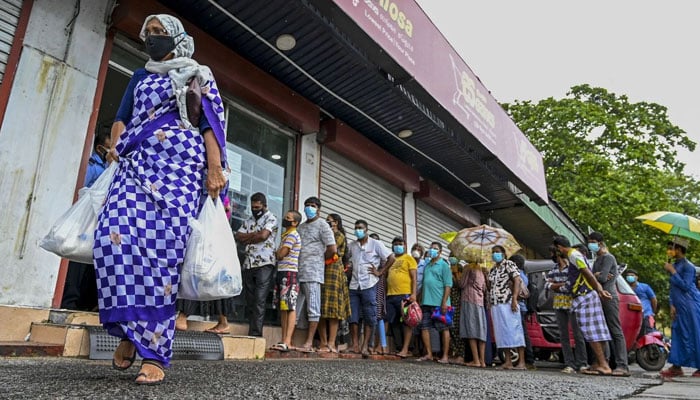 A woman carrying food bags walks past pepole queuing outside a state-run supermarket to buy essential food items in Colombo, Sri Lanka, on September 3. - AFP