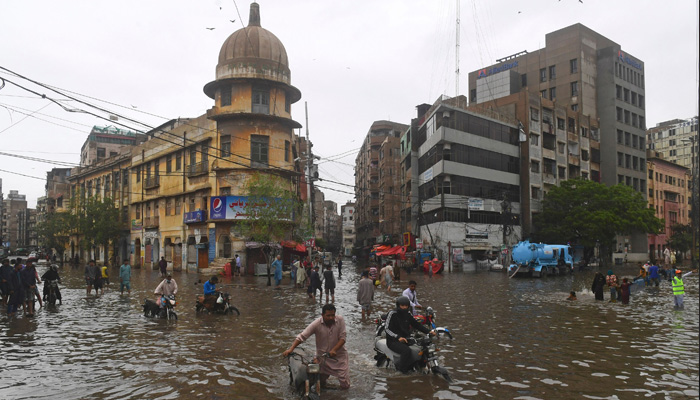 People wade across a flooded street after heavy monsoon rainfall in Karachi on July 25, 2022. -AFP