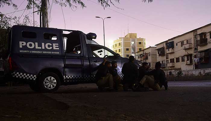 Security personnel take position behind a police vehicle near site of an attack to a police compound in Karachi on February 17, 2023. — AFP