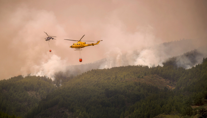 Helicopters fly over the area of Pico Cho Marcial in Arafo to drop water over a huge wildfire raging through forested areas, on the Canary Island of Tenerife, on August 20, 2023. — AFP