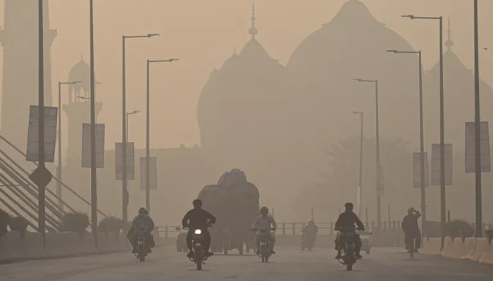 Commuters ride along a road amid smoggy conditions in Lahore on November 16, 2021. — AFP