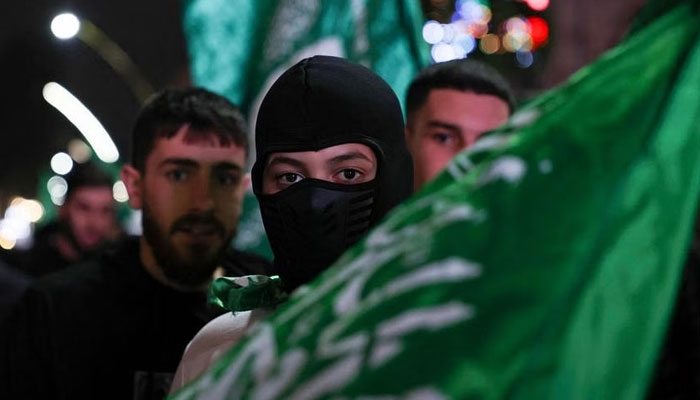 A masked man carries the flag of the Palestinian Hamas movement during a march in the occupied West Bank city of Hebron, to express solidarity with the Gaza Strip. PHOTO: AFP