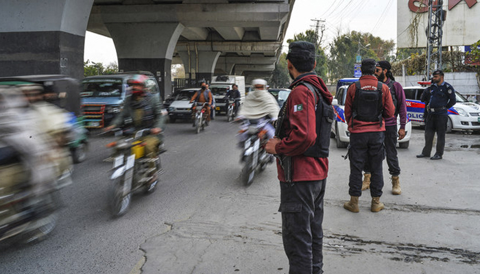 Policemen stand guard as traffic flows on a road in in Peshawar on February 1, 2023. — AFP