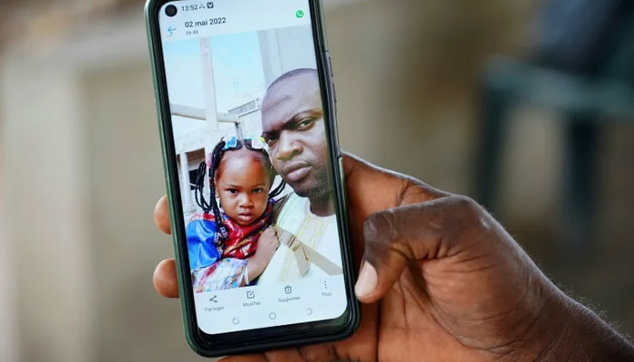 Wuri Bailo Keita, 33, holds a mobile phone showing a picture of himself and his late daughter, Fatoumatta, who is believed to have died of acute kidney failure after ingesting contaminated cough syrup manufactured in India on October 10, 2022. — AFP