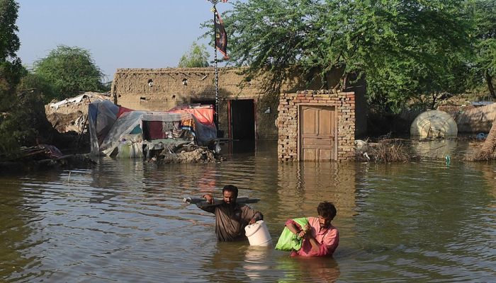 People walk with belongings in the water amid deadly floods in 2022 in Pakistan. — AFP/File