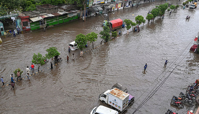 People make their way through a waterlogged road after a heavy rainfall in Lahore on June 26, 2023. — AFP