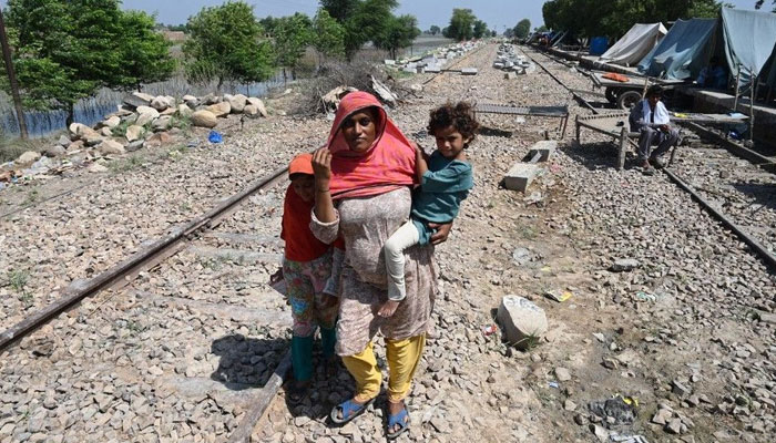 Fahmidah, a pregnant flood-affected woman carries her child as she walks near her tent at a makeshift camp along a railway track in Fazilpur, Rajanpur district of Punjab province on September 3, 2022. — AFP