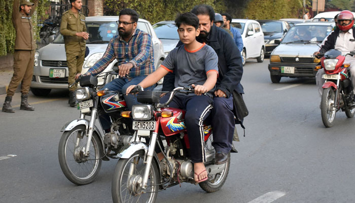 A young boy is riding a motorcycle with his father seated with him on the way to a road in Lahore in November 19, 2023. —  Online