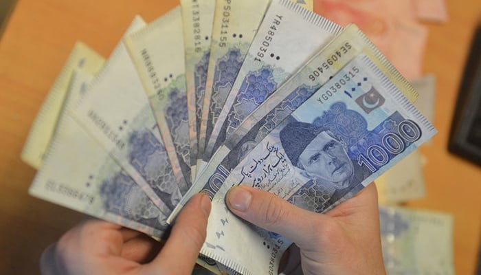 A money changer counts Pakistans currency at a market in Karachi. — AFP/File