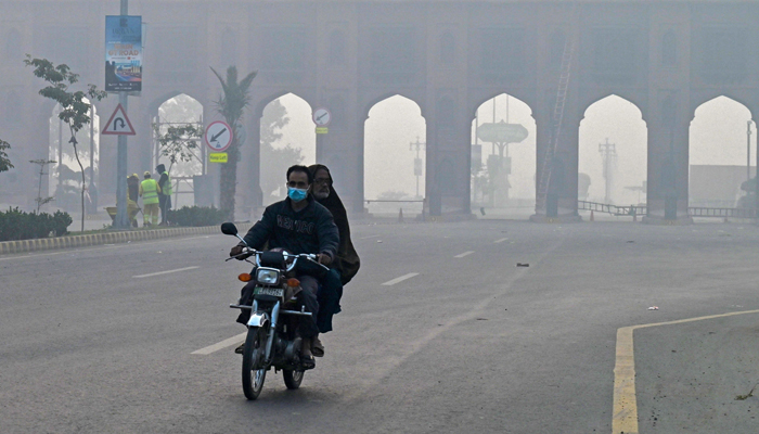 Men ride a motorbike along a road amid dense smog in Lahore on November 24, 2023. — AFP