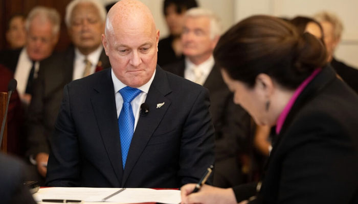 Christopher Luxon (L) looks on as Governor General Dame Cindy Kiro signs documents which formally made him Prime Minister of New Zealand on Monday. — AFP