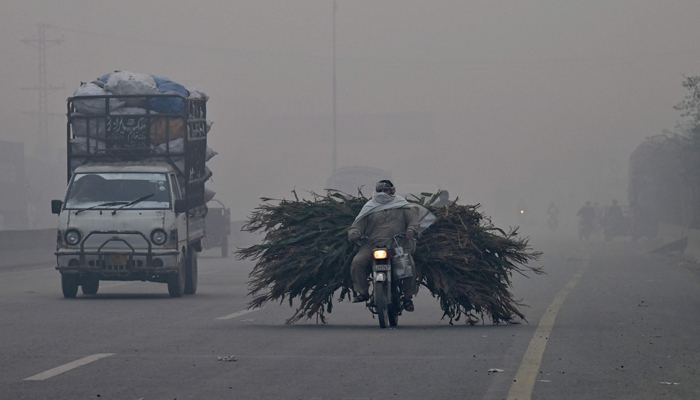 Commuters ride vehicles along a street, amid heavy smog conditions in Lahore on November 24, 2023. — AFP