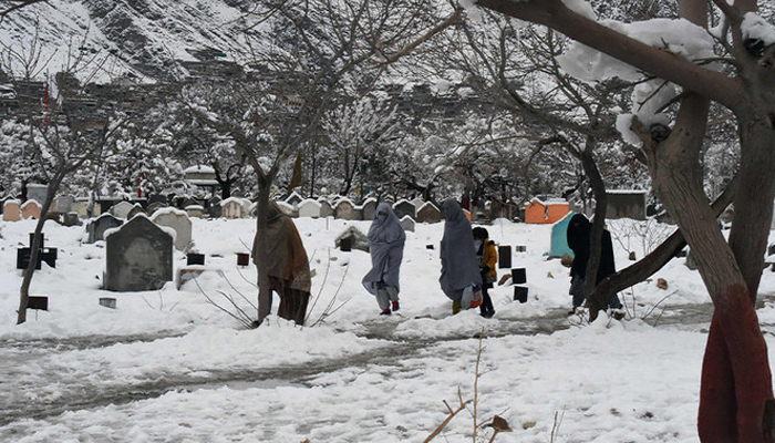 People walk past graves after heavy snowfall. — AFP/File