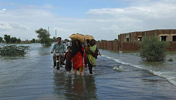 Stranded people wade through a flooded area after heavy monsoon rainfall in Rajanpur. — AFP