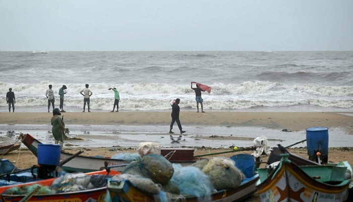 People stand ashore as waves lash over the Kovalam beach after cyclone Michaung made landfall, in Chennai on December 3, 2023. — AFP