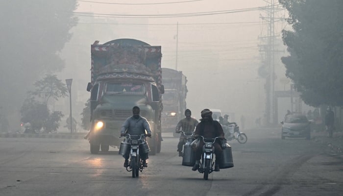 Commuters make their way along a street amid dense smog in Lahore on December 4, 2023. — AFP