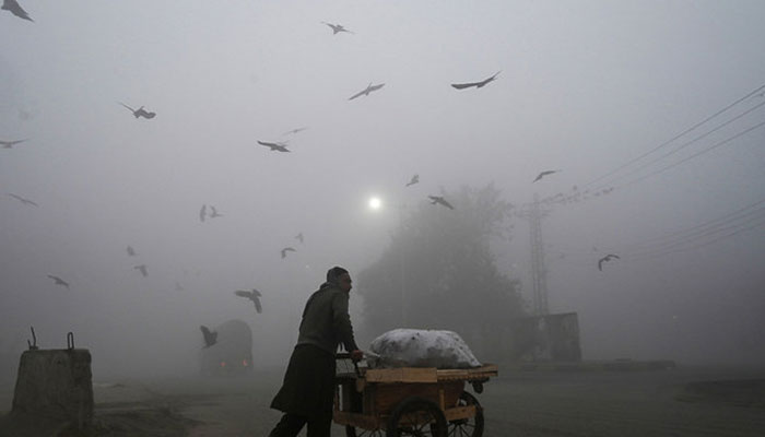 A vendor pushes his cart along a street amid heavy foggy conditions in Lahore, Pakistan. — AFP/File