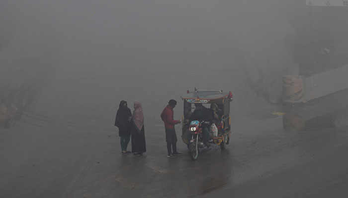 People stand by a road as another converse with a motorcycle-rickshaw driver amid heavy smog on the outskirts of Lahore on December 14, 2023. — AFP