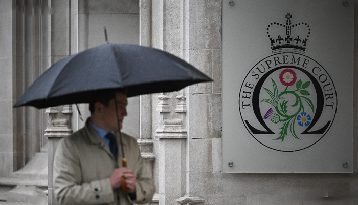 A person holding an umbrella walks past the UK Supreme Court sign in London. — X/@AFP