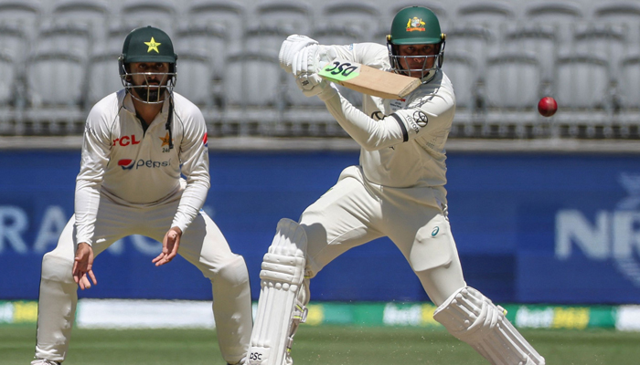 Australias Usman Khawaja (R) plays a shot as Pakistans Agha Salman looks on on day four of the first Test cricket match between Australia and Pakistan in Perth on December 17, 2023. — AFP