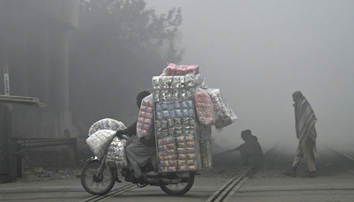 A vendor transporting packets of snacks, crosses a railway track on a foggy winter morning in Lahore on December 28, 2023. — AFP