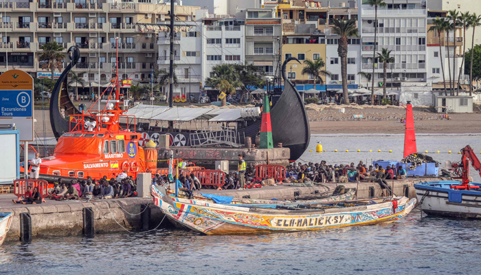 Migrants sit on the pier after arriving aboard two boats at the port of Los Cristianos, in Tenerife, on October 23, 2023. — AFP