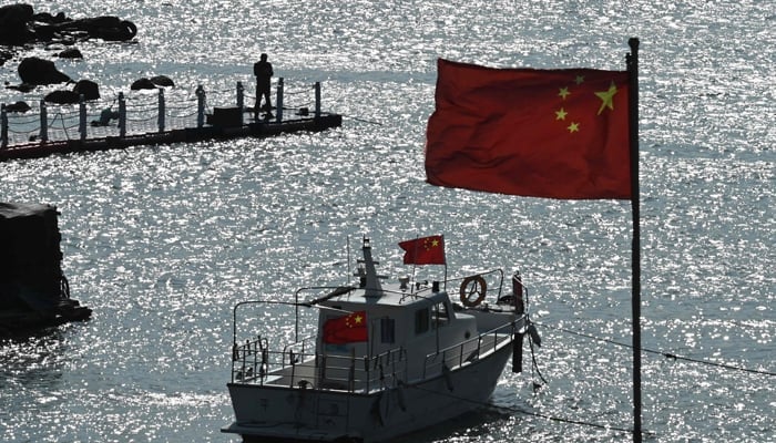 A man stands on a jetty behind a tourist boat and Chinese flags on Pingtan island, opposite Taiwan, in Chinas southeast Fujian province on April 9, 2023. — AFP