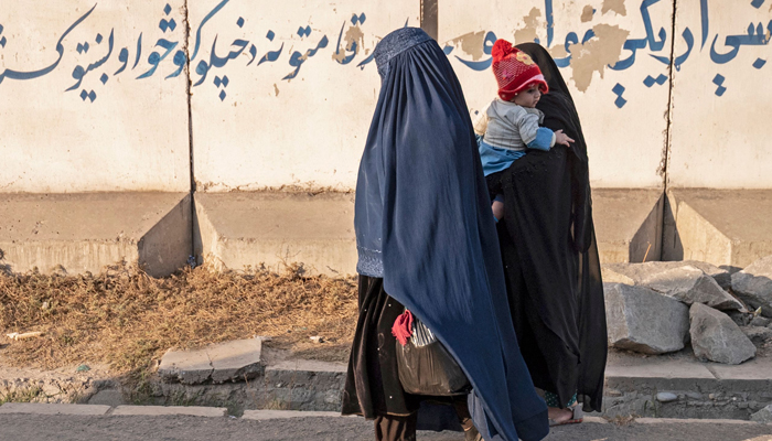 In this photo taken on October 30, 2023, Afghan women with a child walk along a street in Jalalabad. — AFP