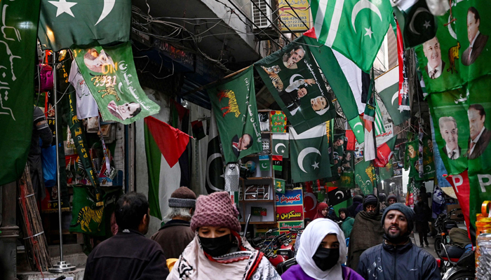 People walk past flags of Pakistans political parties displayed for sale at a market in Lahore on January 13, 2024, ahead of the country´s general elections. — AFP