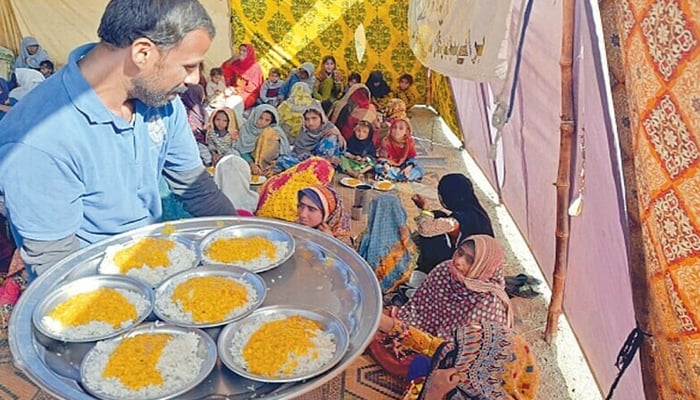 A volunteer distributes food among flood-affected people near a makeshift camp in Dera Allah Yar in Jaffarabad. — AFP/file