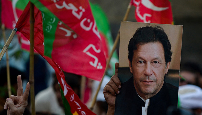 Pakistan Tehreek-e-Insaf (PTI) activists and supporters hold PTI flags and the founder of PTIs poster. — AFP/File