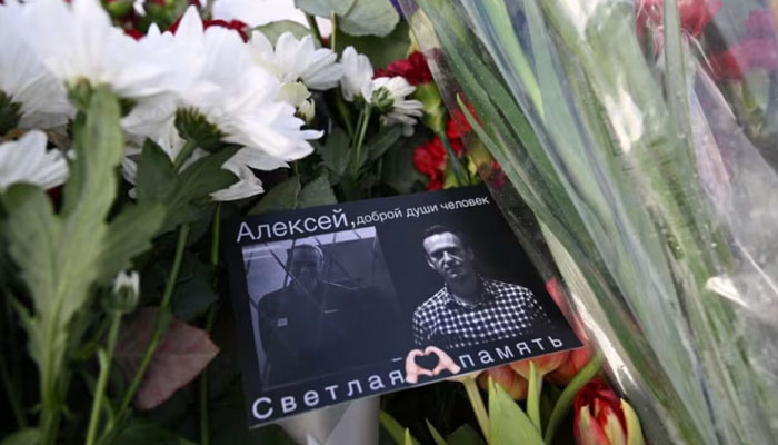 A card with images of late Russian opposition leader Alexei Navalny is seen among flowers left at the Solovetsky Stone in Moscow on February 20, 2024. — AFP