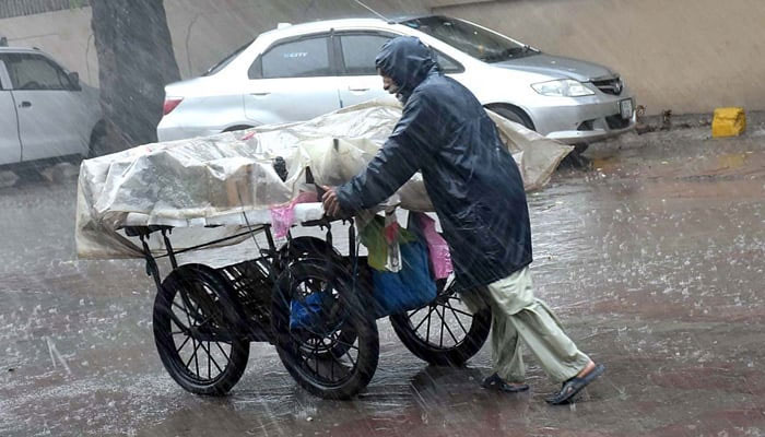 A street vendor pushing his handcart loaded with vegetables during heavy rain. — APP/File