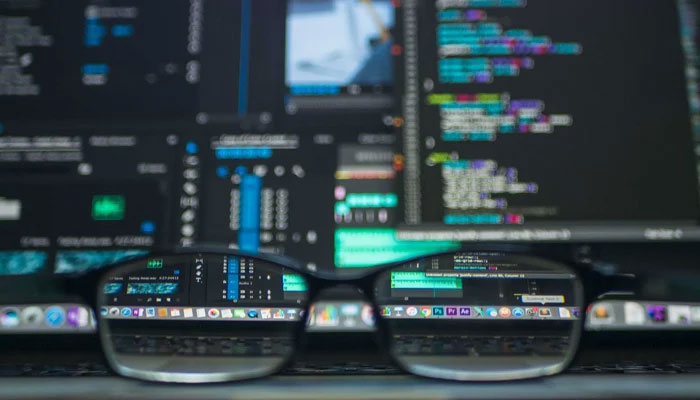 This representational image shows the glasses lens showing tabs on a computer screen displaying information and coding. — Unsplash/File