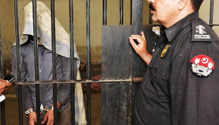 A handcuffed suspect stands behind bars with a policeman standing outside the jail in this undated image. — AFP/File