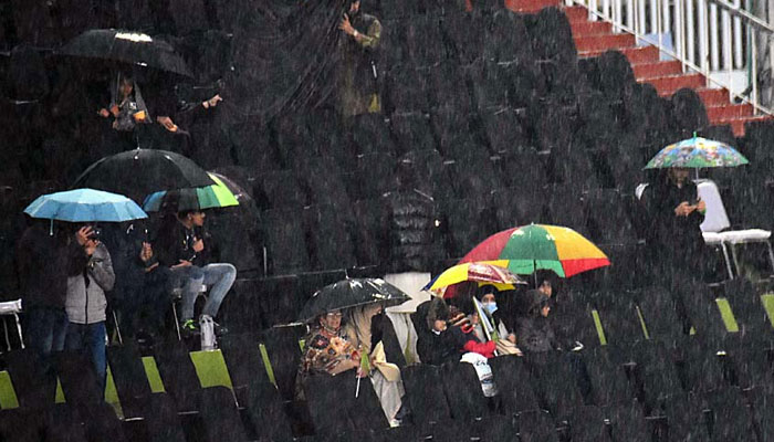 Cricket fans cover them with umbrellas to protect from rain at Rawalpindi Cricket Stadium on March 2, 2024. — APP