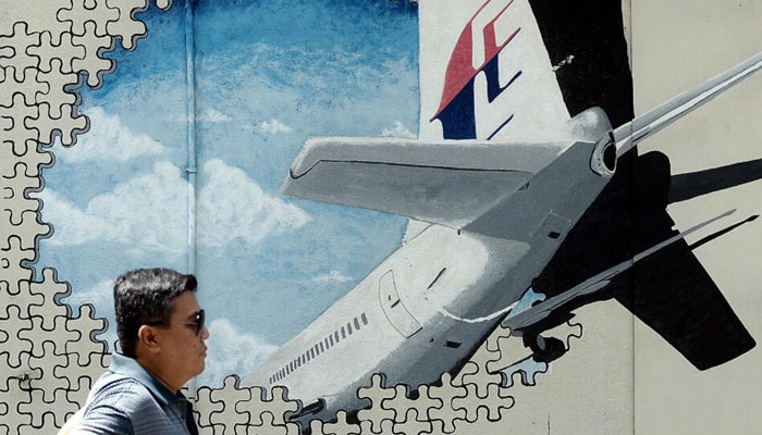 In this photo, a man stands next to a poster of the Flight MH370. — AFP/File