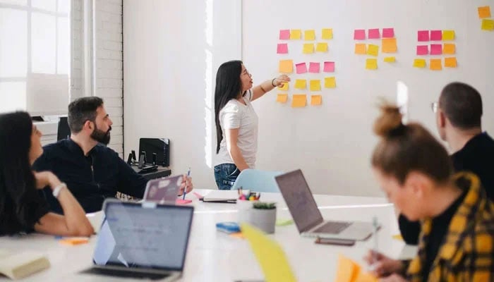 This representational image shows a woman giving a presentation at an office. — Unsplash