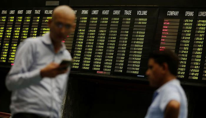 Men use their cell phones as they stand in front of electronic board displaying share market prices during a trading session in the halls of Pakistan Stock Exchange (PSX) in Karachi. — Reuters/File