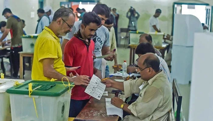 People stand in line up as election officials check their ballot papers during voting general election at a polling station. — AFP/File