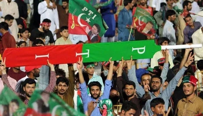 Supporters of former prime minister Imran Khan hold a giant cricket bat with the colours and initials of the party in Multan on July 20, 2018. — AFP