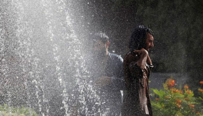 Labourers cool off, as they receive mist from a water fountain along a road during hot and humid weather. — Reuters/File