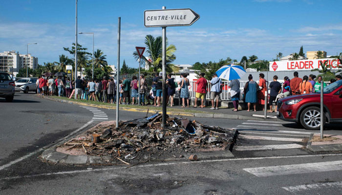 People wait in line to buy provisions from a supermarket as charred items previously set on fire are seen following overnight unrest in the Magenta district of Noumea, Frances Pacific territory of New Caledonia, on May 18, 2024. — AFP