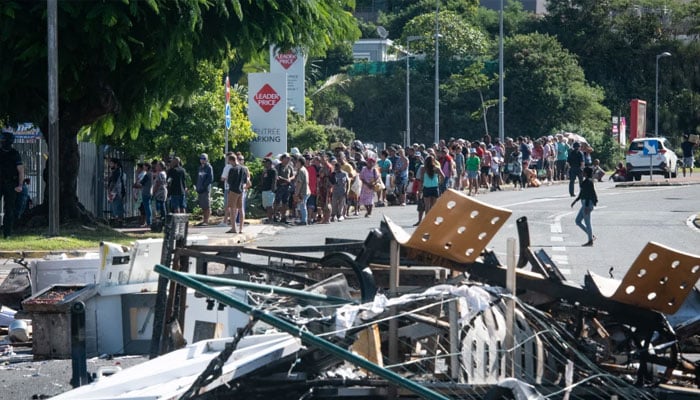 People wait in line to buy provisions from a supermarket along a street blocked by debris and burnt out items following overnight unrest in the Magenta district of Noumea, Frances Pacific territory of New Caledonia, on May 18, 2024. — AFP