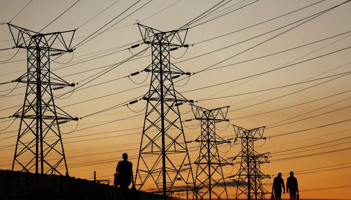 Locals walk past electricity pylons. — Reuters/File