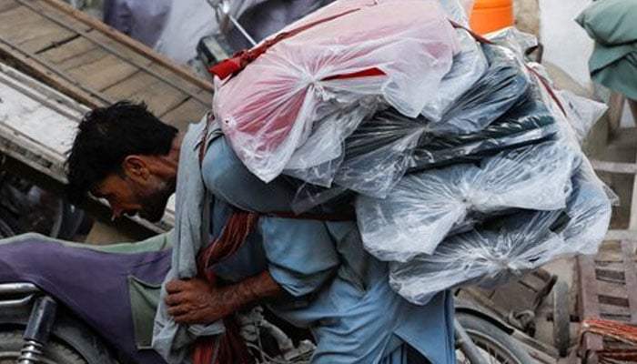 A labourer bends over as he carries packs of textile fabric on his back to deliver to a nearby shop in a market in Karachi on June 24, 2022. — Reuters