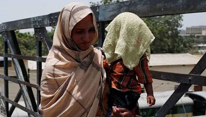 A mother holds her child whos covered with a cloth as a protective measure against heatwave. — Reuters/File