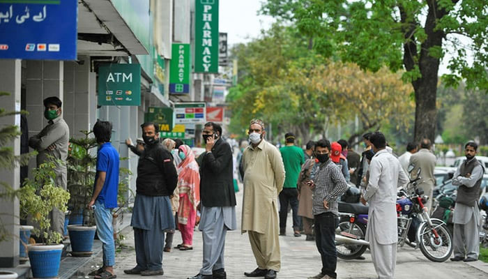 People wait for their turn to withdraw money outside a bank in Islamabad. —AFP/File