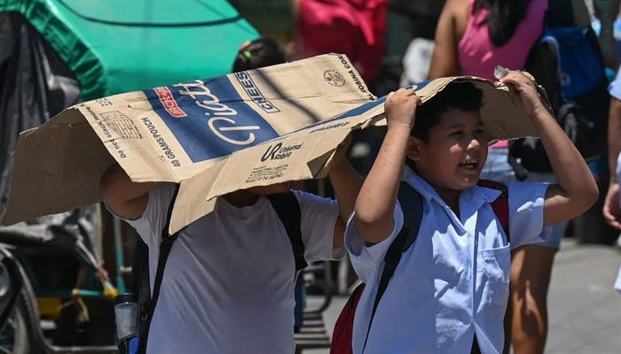 Students use cardboard to protect themselves from the sun during a hot day. — AFP/File