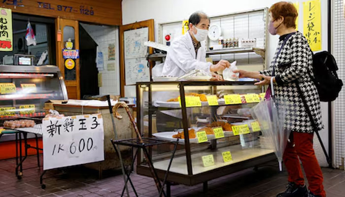 A customer buys food at a shop selling cooked food at a market in Tokyo, Japan, March 24, 2023. — Reuters